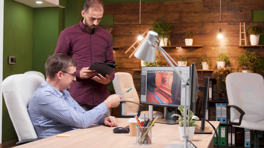 graphic-designer-working-in-gaming-industry-showing-new-virtual-game-design-to-his-colleague-discussing-level-environment-team-of-gaming-production-developing-3d-videogame-in-creativity-office
