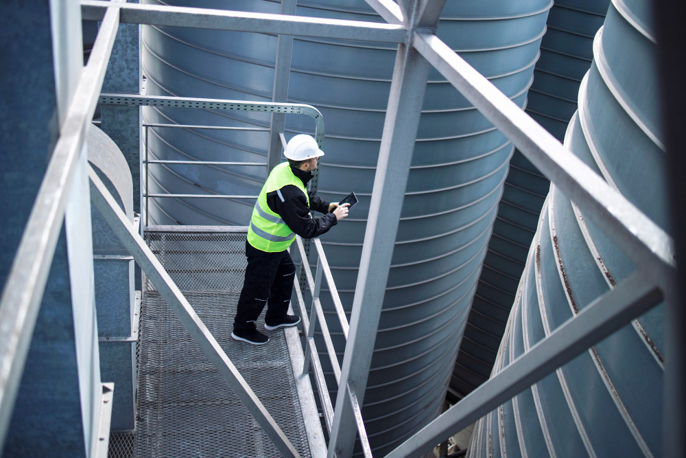 factory-silos-worker-standing-on-metal-platform-between-industrial-storage-tanks-and-looking-at-tablet-about-food-production