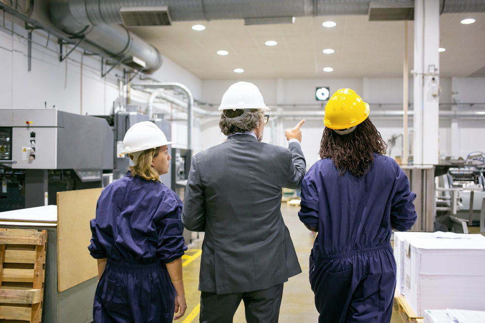 male-engineer-female-factory-employees-hardhats-walking-plant-floor-talking-man-pointing-equipment-instructing-women