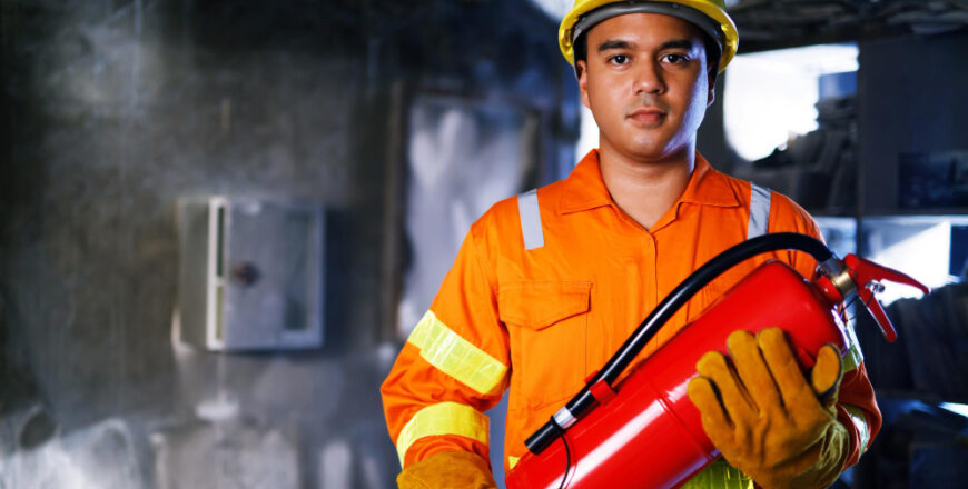 fireman-hand-holding-fire-extinguisher-available-in-emergencies-conflagration-damage-background-safety-concept